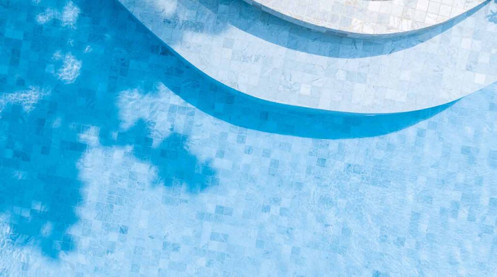 A close-up view of crystal-clear pool water over a premium pebble interior finish, highlighting the smooth texture, durability, and vibrant watercolor of a custom Orange County pool.
